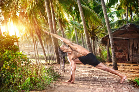 Yoga Parivrtta Parsvakonasana horizon pose by fit man with dreadlocks on the beach near the fishermen hut in Varkala, Kerala, India Stock Photo Yoga Parivrtta Parsvakonasana horizon pose by fit man with dreadlocks on the beach near the fishermen hut in Varkala, Kerala, India Stock Photo - 14625044