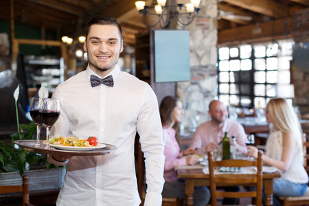 restaurant interior: Portrait of a happy male waiter with a tray in his hand at the restaurant