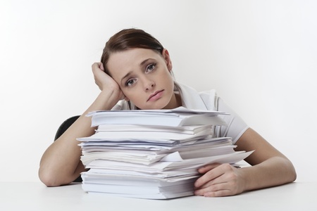 A stressed female, sitting at her desk with a large pile of papers stack in front of her Stock Photo