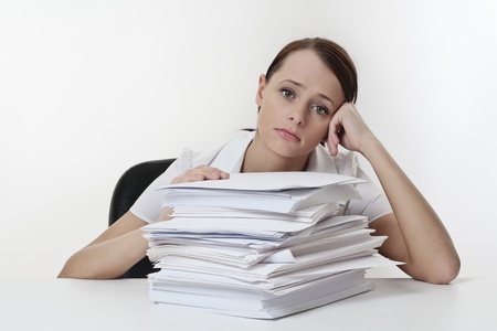 A stressed female, sitting at her desk with a large pile of papers stack in front of her Stock Photo
