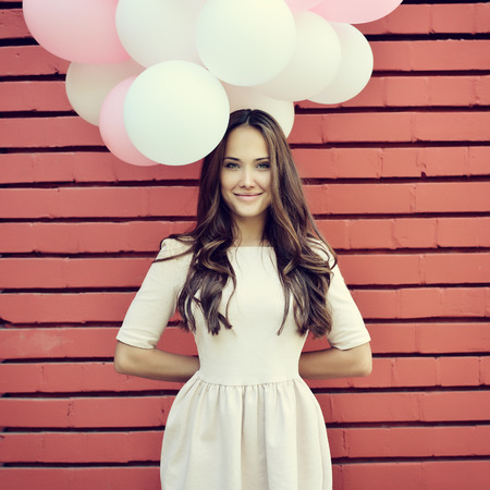 balloon: Happy young woman standing over red brick wall and holding pink and white balloons. Pleasure. Dreams. Toned.