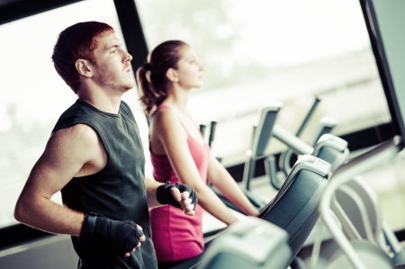 Running on treadmill in gym or fitness club - group of women and men exercising to gain more fitness