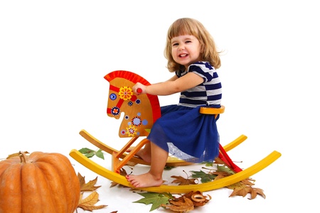 Niña feliz sentada en sul caballo de madera, al lado de la calabaza y sobre las hojas. Niña feliz sentada en sul caballo de madera, al lado de la calabaza y sobre las hojas.