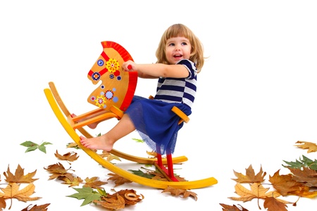 Una niña sonriente que monta su caballo de madera, en el piso hay hojas amarillas. Una niña sonriente que monta su caballo de madera, en el piso hay hojas amarillas.