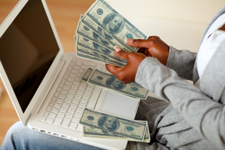 Portrait of a black woman counting plenty of cash money in front a laptop at home indoor Stock Photo