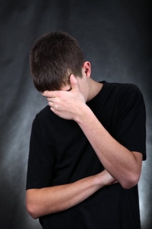 deep thinking: Sad Young Man On the Black Background hide his Face
