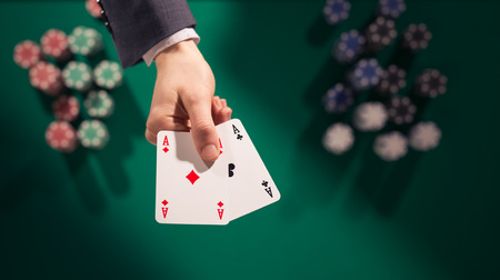 poker: Elegant male poker player holding two aces with stacks of chips on background and green table, top view Stock Photo