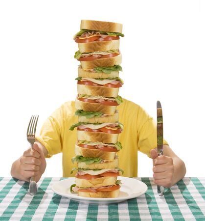 Giant sandwich on a white plate, with hands holding a a knife and fork on a table cloth. Stock Photo