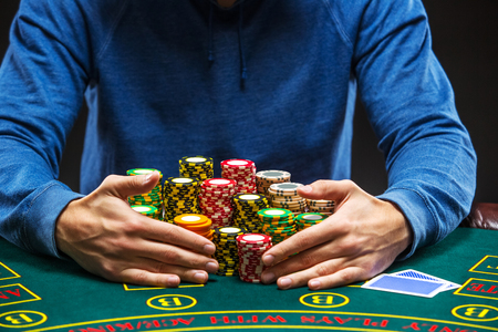 poker: Poker player sitting at a poker table taking poker chips after winning. Close up