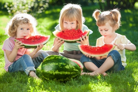 Grupo de niños felices comiendo sandía en la hierba verde en el parque de verano. Grupo de niños felices comiendo sandía en la hierba verde en el parque de verano.