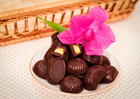 26827662-mazzo-di-deliziosi-cioccolatini-dolci-su-un-piattino-con-un-fiore-rosa-sullo-sfondo-di-un-cesto-di-v.jpg