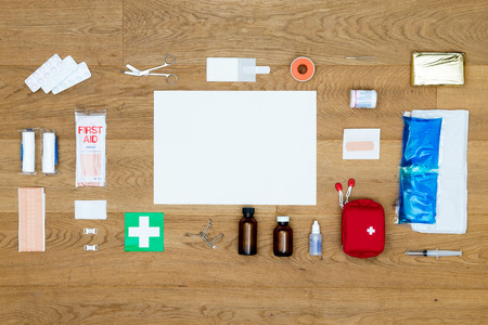 The items and objects in a first aid kit neatly aligned on a wooden surface with a blank card for a message or text as copy space available items include pliers bandages plaster pills heat or cold pack isolation blanket tape and much more Stock Photo