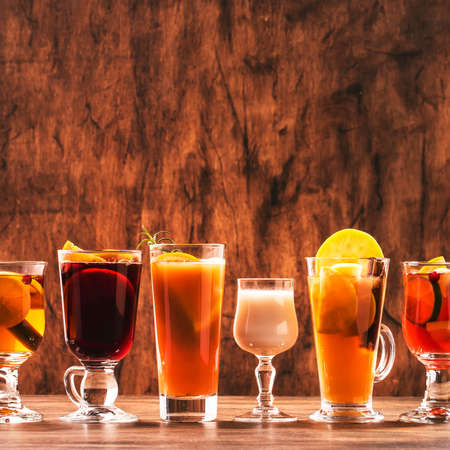 Selection Of Autumn Or Winter Alcoholic Hot Drinks And Cocktails - Mulled Wine, Glogg, Grog, Eggnog, Warm Ginger Ale, Hot Buttered Rum, Punch, Mulled Apple Cider On Wood Background, Copy Space