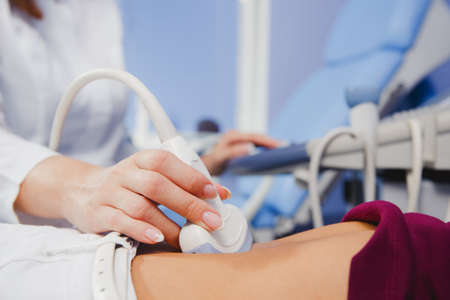 Female doctor operating ultrasound scanner examining belly of her female patient