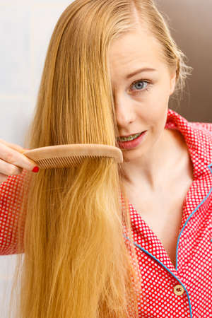 木製櫛付きのバスルームで彼女の長い滑らかな髪をブラッシングを梳く女