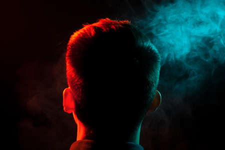 The view from the back of the smoker’s head is highlighted in red and out of the green smoke raising his face up. harm to human health.
