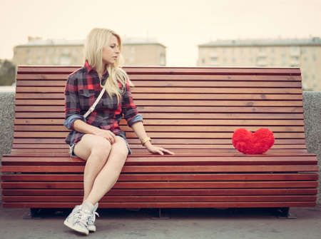 sad lonely: Sad lonely girl sitting on a bench near to a big red heart Stock Photo
