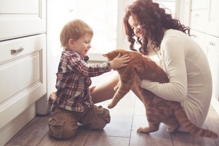 Mother with her baby playing with pet on the floor at the kitchen at home Фото со стока