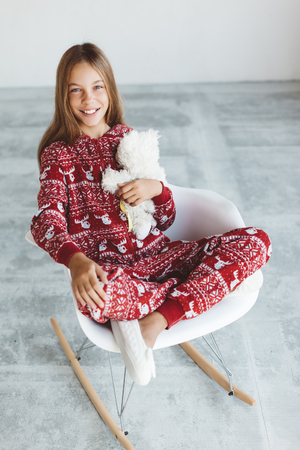10 年古い子供服を着て暖かいクリスマス パジャマ コンクリート北欧インテリアでモダンなロッキングチェアに座っています 怠惰な冬の朝 快適なシーン の写真素材 画像素材 Image