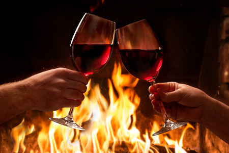 Hands toasting wine glasses in front of lit fireplace Stock Photo