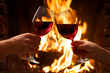 Hands toasting wine glasses in front of lit fireplace Фото со стока