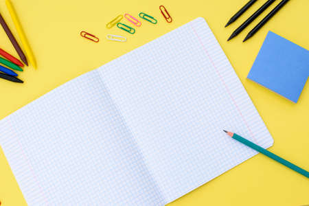 Notebook in a cage with a pencil, eraser, ruler, paper clips and other office supplies on a yellow background. concept back to school. place for text. Stock Photo