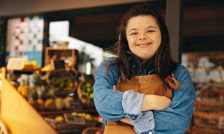Employé de magasin atteint du syndrome de down souriant à la caméra alors qu'il se tenait dans une épicerie. femme autonome ayant une déficience intellectuelle travaillant dans un supermarché local.