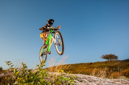Cyclist in helmet and glasses jumping on a mountain bike on the hill against blue sky. Dangerous downhill. Bottom view