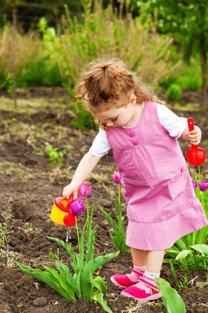 Cute curly girl watering flowers in the garden Фото со стока