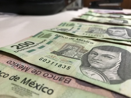 Many mexican pesos bills distributed and spread on a beige colored desk