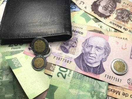 Many mexican pesos bills spread over a wooden desk inside a small business office