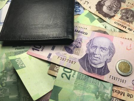 Many mexican pesos bills spread over a wooden desk inside a small business office