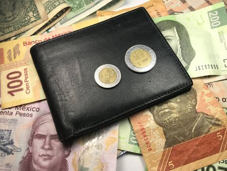 Many mexican pesos and other latin american money bills spread over a wooden desk inside a small business office