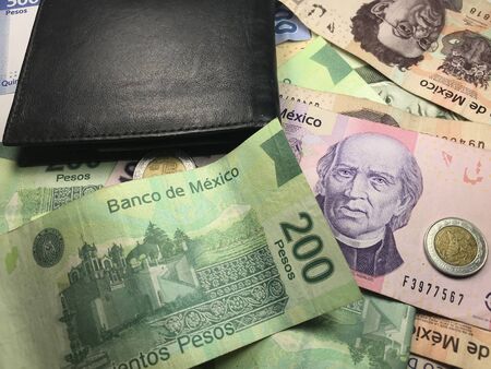 Many mexican pesos bills spread over a wooden desk inside a small business office Stock Photo