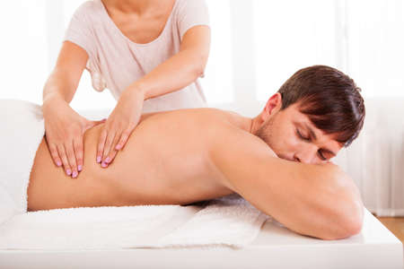 Massage: Красивый молодой человек лежал на животе в спа, имеющие массаж спины Фото со стока