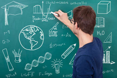 male teacher teaching physic equation on chalkboard in classroom