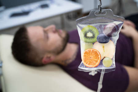 Mężczyzna w szpitalu otrzymujący dożylną infuzję plasterków owoców w torebce z solą fizjologiczną Zdjęcie Seryjne