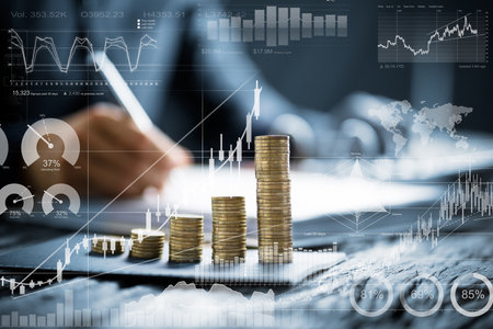 Midsection of businessman calculating invoice with stacked coins arranged at office desk
