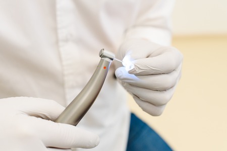 hand of dentist in white latex gloves holding dental drill machine