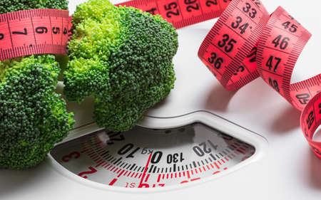 Suivre un régime sain manger mince concept de contrôle de poids. Closeup vert brocoli avec ruban à mesurer sur les échelles blanches Photo