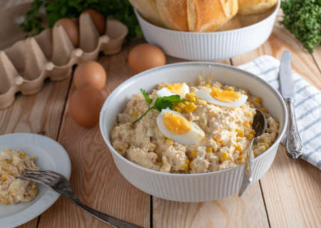 Salade de thon avec mayonnaise, œufs durs, maïs et oignons. servi dans un bol rustique blanc avec des petits pains sur un fond de table en bois. cuit maison et prêt à manger. Banque d'images