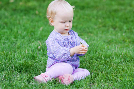 牧草地の草の上に座ってカラフルな服でかわいい赤ちゃんおかしい女の子 の写真素材 画像素材 Image