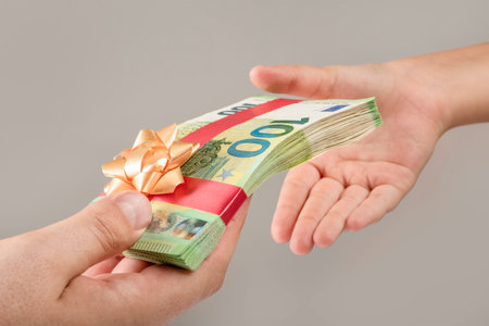 L'argent comme cadeau, prix ou bonus. un homme donne un paquet d'argent à un enfant. les billets de 100 euros sont attachés avec un ruban rouge avec un arc.