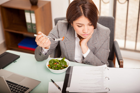 Beschäftigte junge Geschäftsfrau, die ein gesundes Mittagessen beim Arbeiten in ihrem Büro isst Foto auf Lager