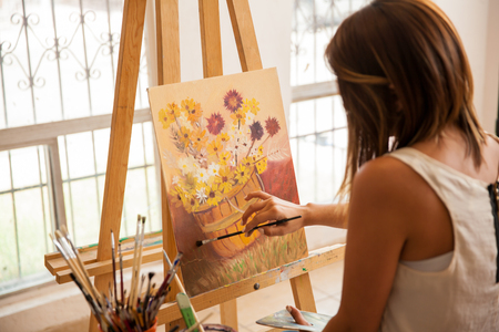Rear view of a pretty female artist giving the finishing touches to her latest painting
