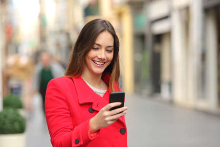 Girl walking and texting on the smart phone in the street wearing a red jacket in winter