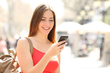 Woman walking and using a smart phone in the street in a sunny summer day
