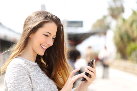 Happy girl texting on a smart phone in a train station while is waiting Stock Photo