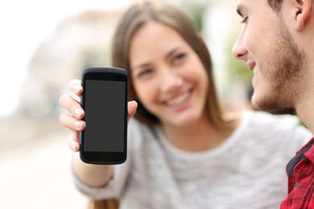 Happy couple showing apps in a blank smart phone screen outdoors Stock Photo
