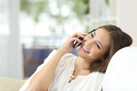 Happy girl talking on the mobile phone resting on a couch at home